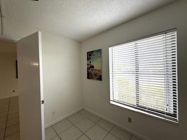 spare room with a textured ceiling, light tile patterned flooring, and baseboards
