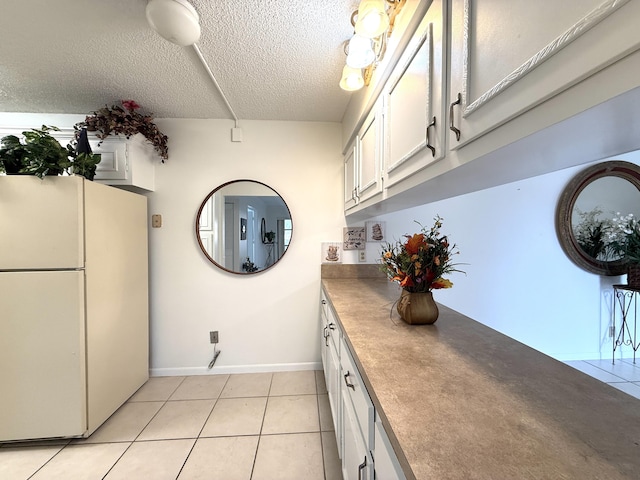 kitchen featuring freestanding refrigerator, a textured ceiling, light tile patterned floors, white cabinetry, and baseboards