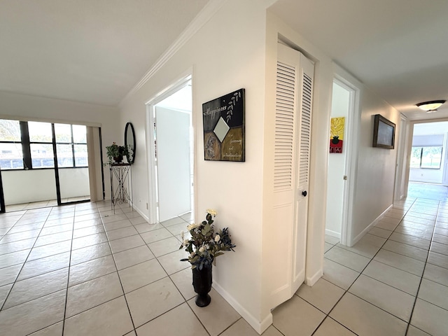 hall with light tile patterned floors, ornamental molding, and baseboards