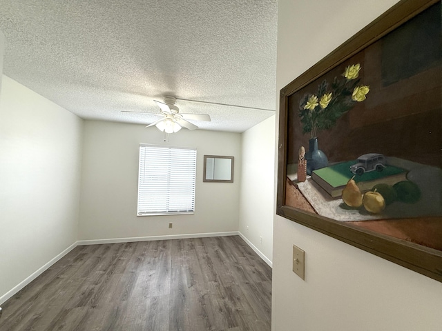 spare room with wood finished floors, ceiling fan, a textured ceiling, and baseboards