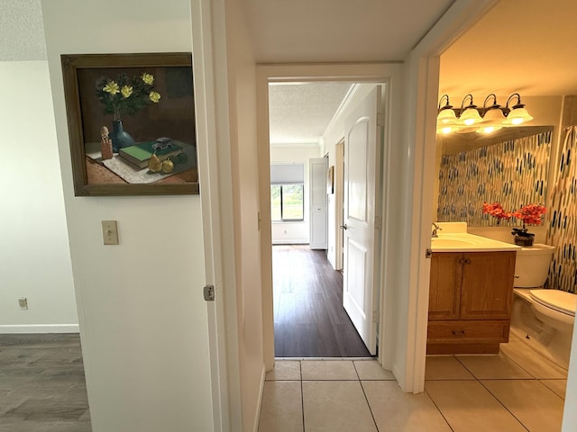 hall with a textured ceiling, light tile patterned floors, a sink, and baseboards