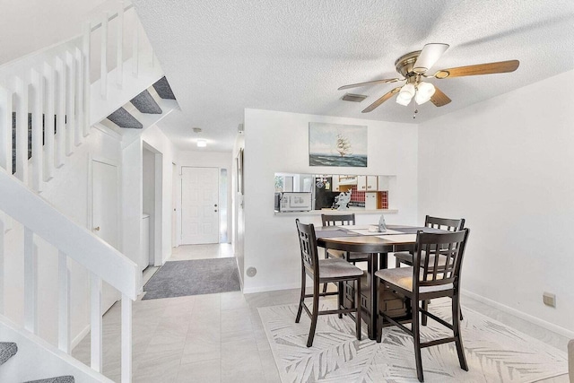 dining area featuring visible vents, stairs, baseboards, a textured ceiling, and a ceiling fan