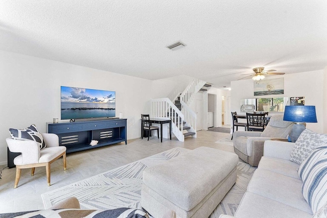 living room featuring stairway, ceiling fan, a textured ceiling, and visible vents