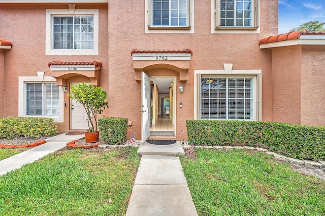 doorway to property with a lawn and stucco siding