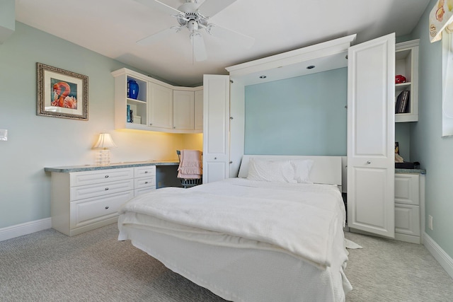 bedroom featuring a ceiling fan, baseboards, light colored carpet, and built in desk