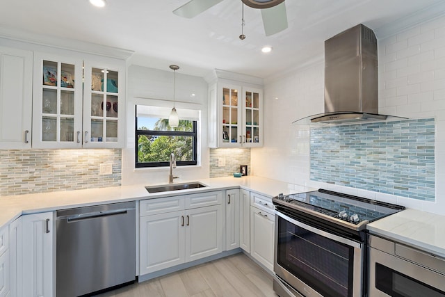 kitchen with wall chimney range hood, appliances with stainless steel finishes, a sink, light countertops, and white cabinetry