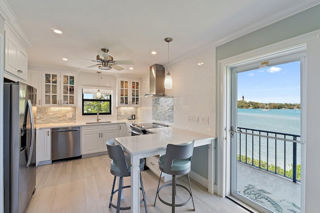kitchen featuring a sink, wall chimney exhaust hood, stainless steel appliances, a peninsula, and decorative backsplash