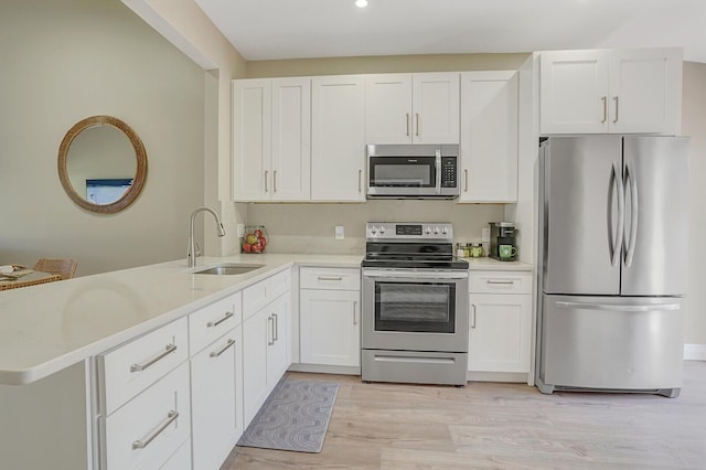 kitchen featuring a sink, a peninsula, stainless steel appliances, light wood-type flooring, and light countertops