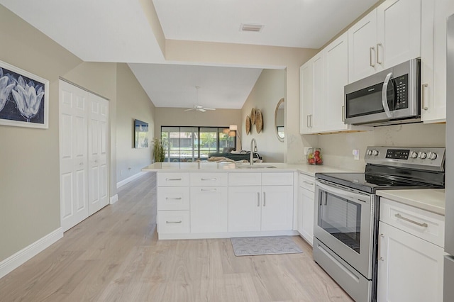 kitchen featuring a peninsula, a sink, light countertops, appliances with stainless steel finishes, and lofted ceiling