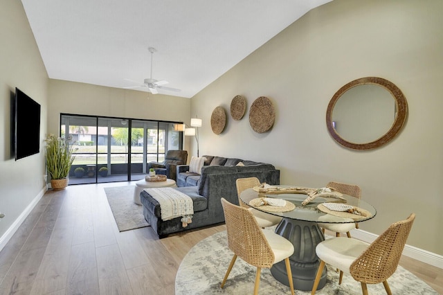 dining space featuring light wood-style flooring, baseboards, ceiling fan, and high vaulted ceiling