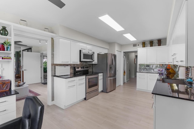 kitchen with stainless steel appliances, dark countertops, tasteful backsplash, white cabinets, and light wood-style floors