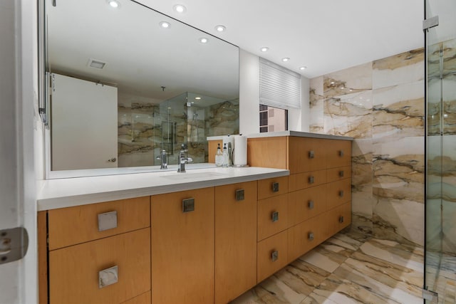 bathroom featuring marble tiled flooring, a marble finish shower, vanity, recessed lighting, and tile walls