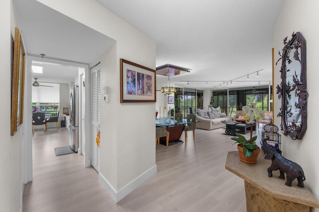 hallway featuring light wood-type flooring, rail lighting, and baseboards