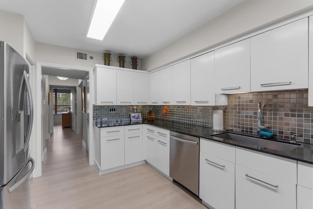 kitchen with appliances with stainless steel finishes, a sink, tasteful backsplash, light wood finished floors, and white cabinetry