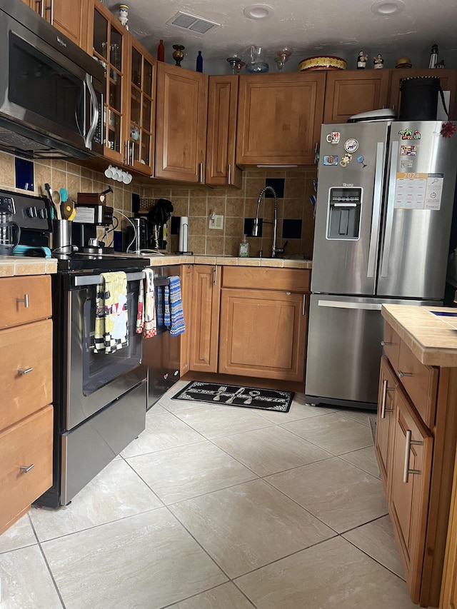 462 Normandy J, Delray Beach, FL 33484 - kitchen featuring glass insert cabinets, stainless steel appliances, visible vents, decorative backsplash, and light tile patterned flooring