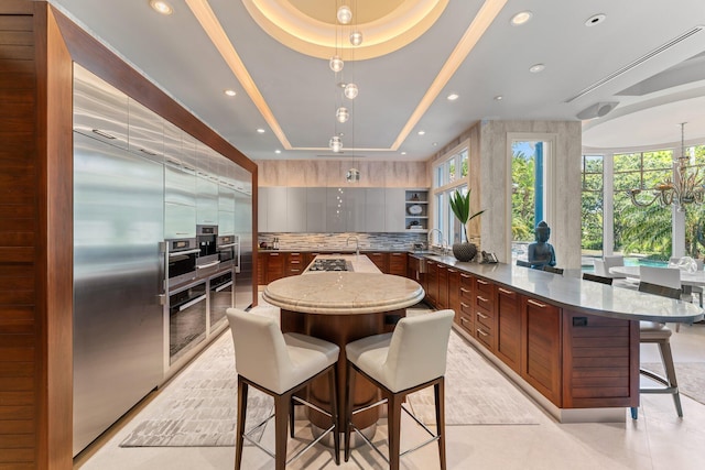 232 Bears Club Dr, Jupiter, FL 33477 - kitchen featuring a tray ceiling, backsplash, a healthy amount of sunlight, and a breakfast bar