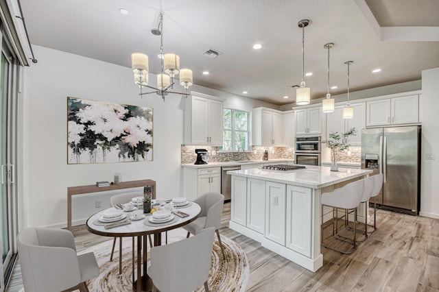 179 Tresana Blvd Unit 145, Jupiter, FL 33478 - kitchen with stainless steel appliances, light wood-type flooring, tasteful backsplash, a kitchen island, and white cabinets