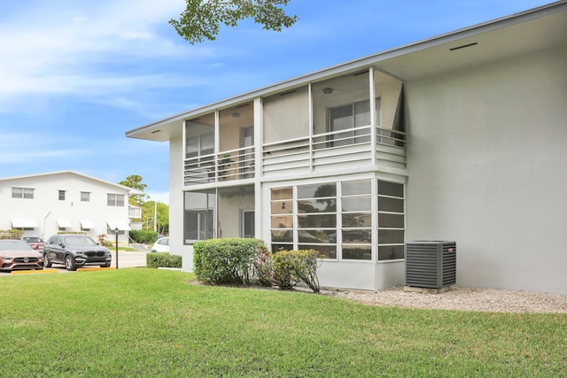 rear view of house with central AC unit, stucco siding, and a yard
