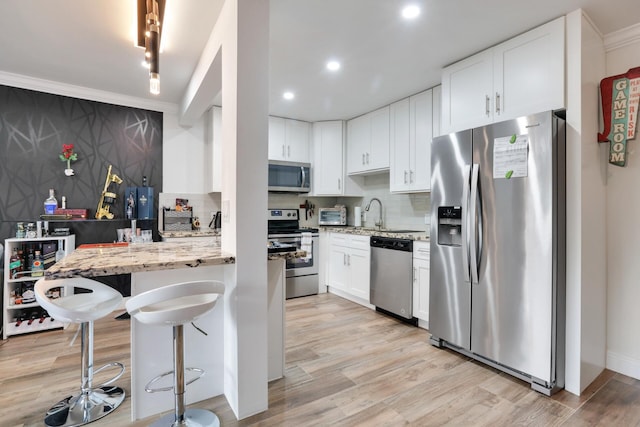 kitchen featuring stainless steel appliances, light stone counters, tasteful backsplash, white cabinets, and crown molding