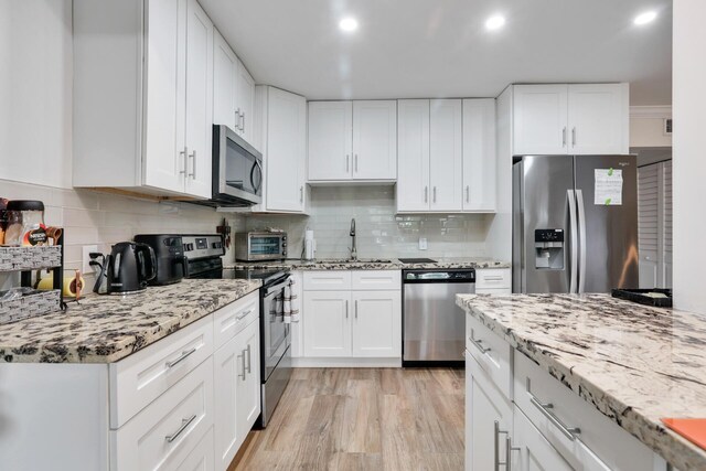 kitchen featuring appliances with stainless steel finishes, a sink, light stone counters, decorative backsplash, and white cabinetry