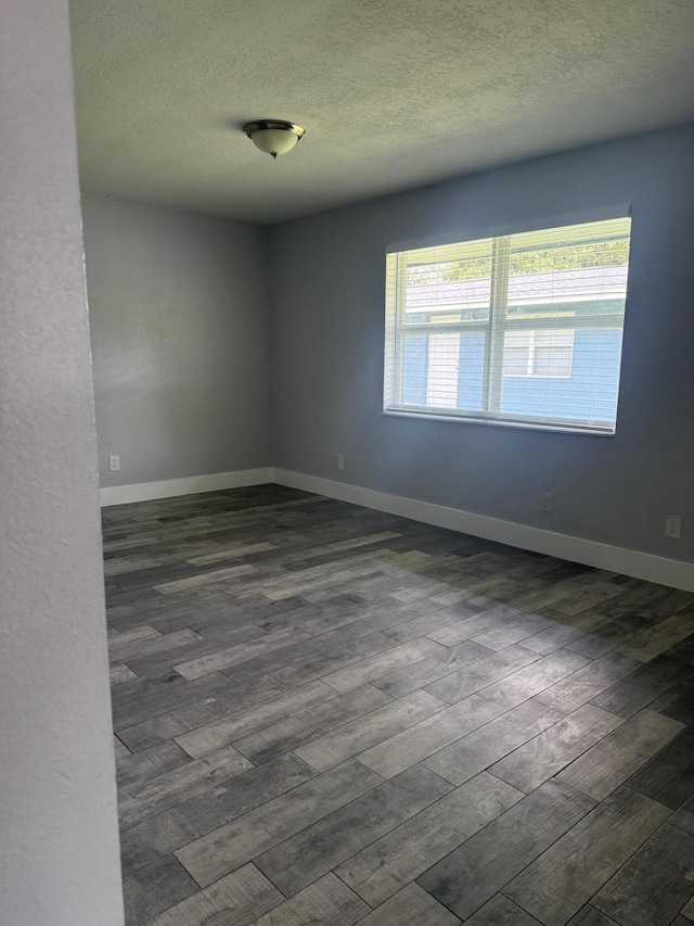 empty room featuring a textured ceiling, dark wood finished floors, and baseboards