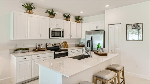 kitchen featuring baseboards, a breakfast bar, a sink, white cabinets, and appliances with stainless steel finishes