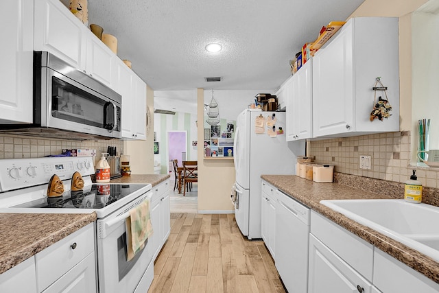 1742 SW Hampshire Ln, Port Saint Lucie, FL 34953 - kitchen featuring white appliances, light wood-style flooring, white cabinetry, decorative backsplash, and a textured ceiling