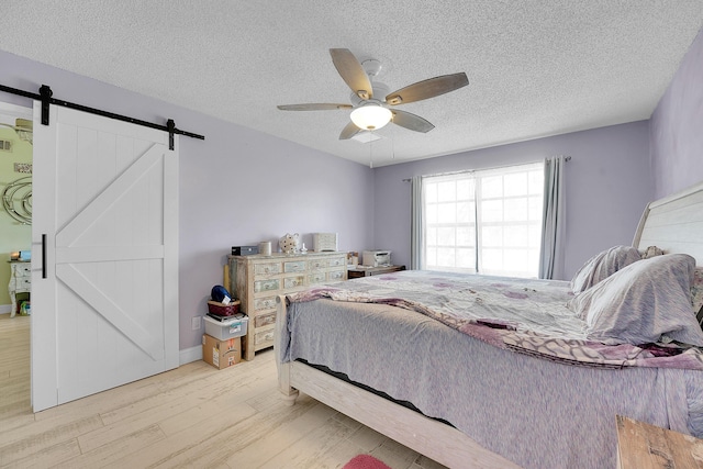 1742 SW Hampshire Ln, Port Saint Lucie, FL 34953 - bedroom with light wood-type flooring, a barn door, a textured ceiling, and ceiling fan