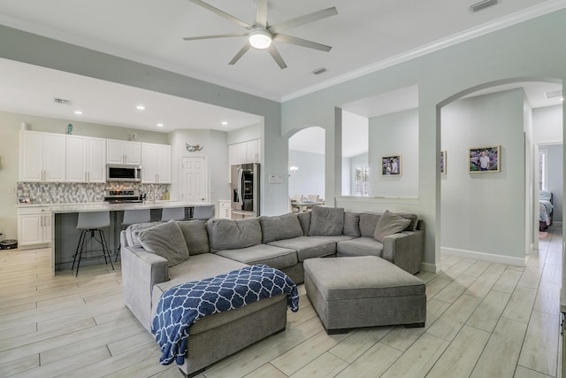 living room with visible vents, crown molding, arched walkways, a ceiling fan, and light wood-style floors