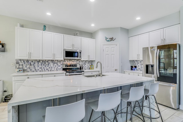 kitchen featuring appliances with stainless steel finishes, a sink, backsplash, white cabinets, and an island with sink