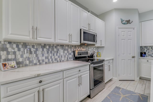 kitchen featuring stainless steel appliances, white cabinets, decorative backsplash, and light stone countertops