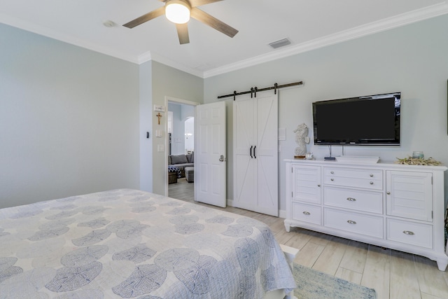 bedroom with light wood-style flooring, a barn door, ornamental molding, ceiling fan, and visible vents