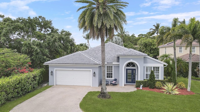 view of front of property with a front yard, stucco siding, an attached garage, and decorative driveway