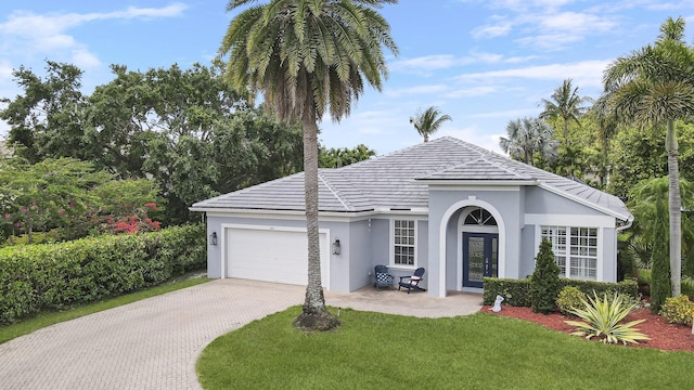 single story home with a garage, stucco siding, a tile roof, a front lawn, and driveway