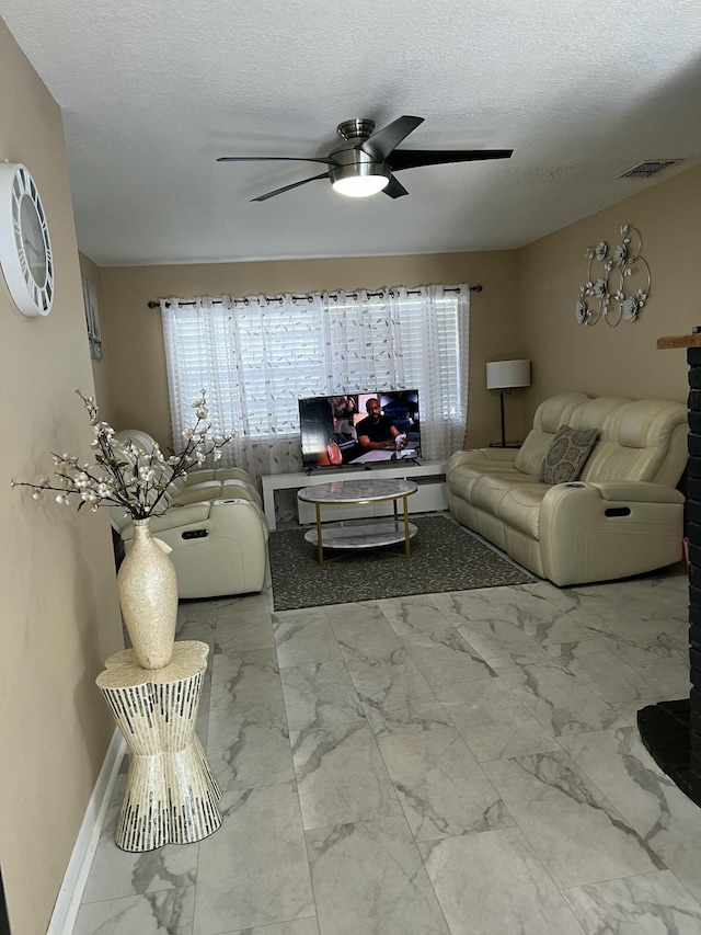 living room with ceiling fan, marble finish flooring, healthy amount of natural light, a textured ceiling, and baseboards