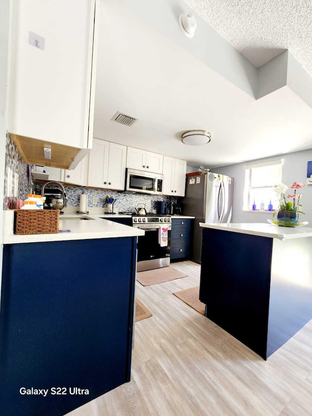 kitchen featuring a peninsula, appliances with stainless steel finishes, visible vents, white cabinets, and light wood-style floors