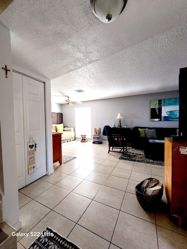 interior space with ceiling fan, a textured ceiling, and light tile patterned flooring