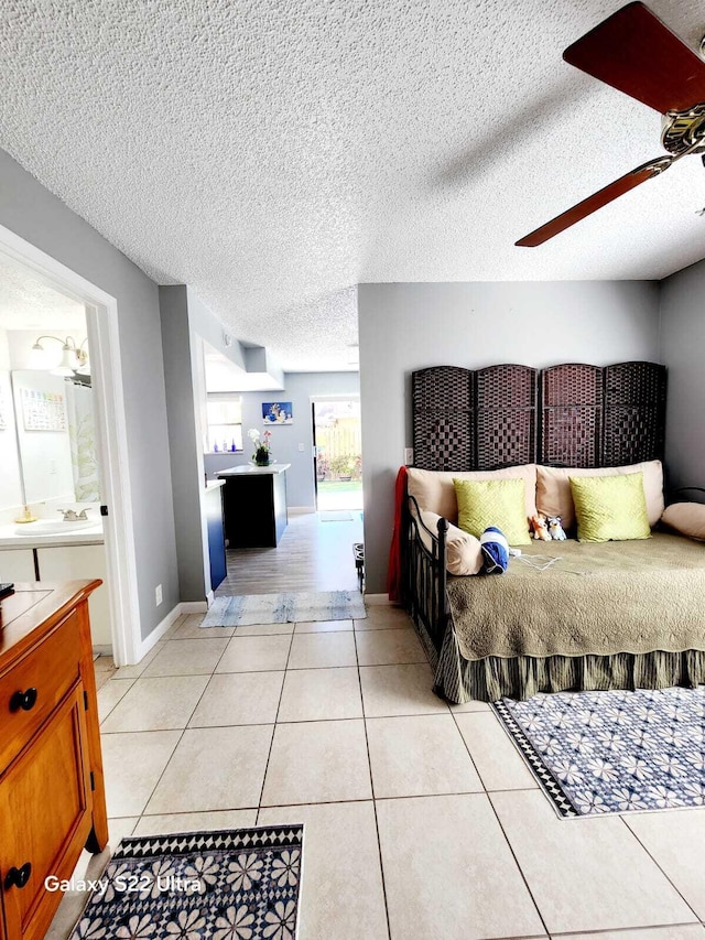 bedroom featuring a textured ceiling, a ceiling fan, light tile patterned floors, connected bathroom, and baseboards
