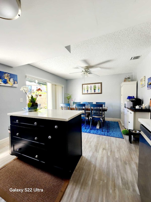 kitchen with a ceiling fan, light countertops, dark cabinets, and light wood-style flooring