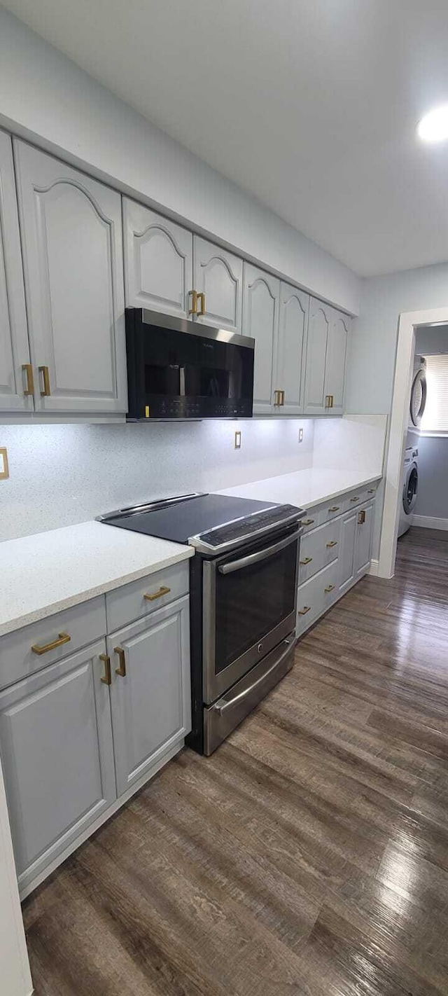 kitchen with stacked washer / dryer, stainless steel electric range, gray cabinetry, and dark wood-type flooring