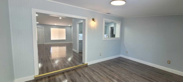 spare room with ornamental molding, baseboards, and dark wood-type flooring