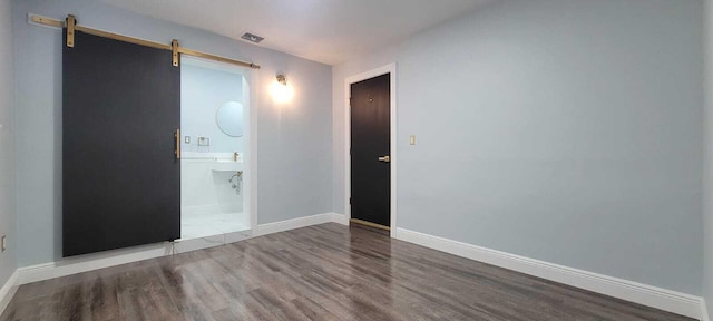 empty room featuring baseboards, a barn door, and wood finished floors