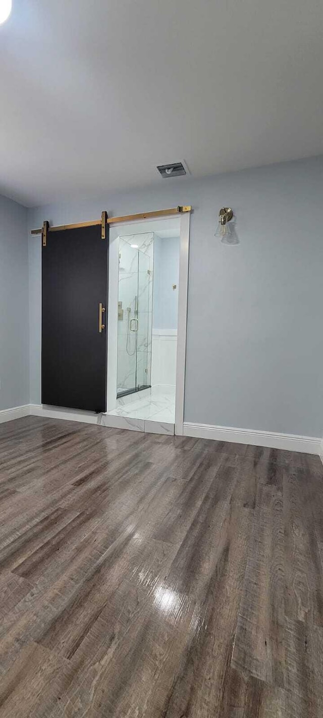 unfurnished room featuring a barn door, baseboards, visible vents, and wood finished floors