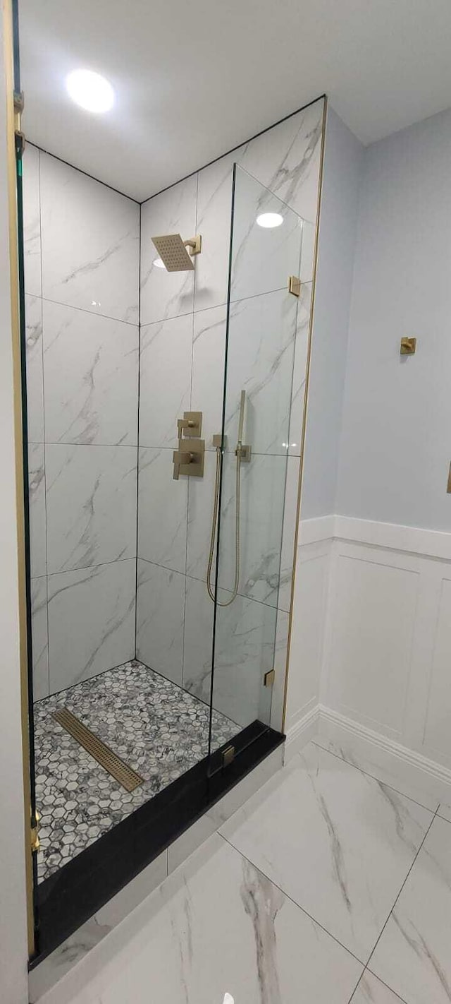 bathroom with a decorative wall, a wainscoted wall, a marble finish shower, and marble finish floor