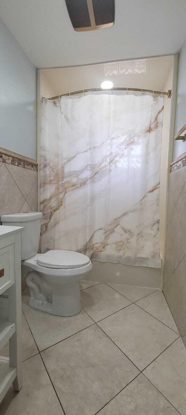 bathroom featuring toilet, a wainscoted wall, a shower with shower curtain, tile walls, and tile patterned flooring
