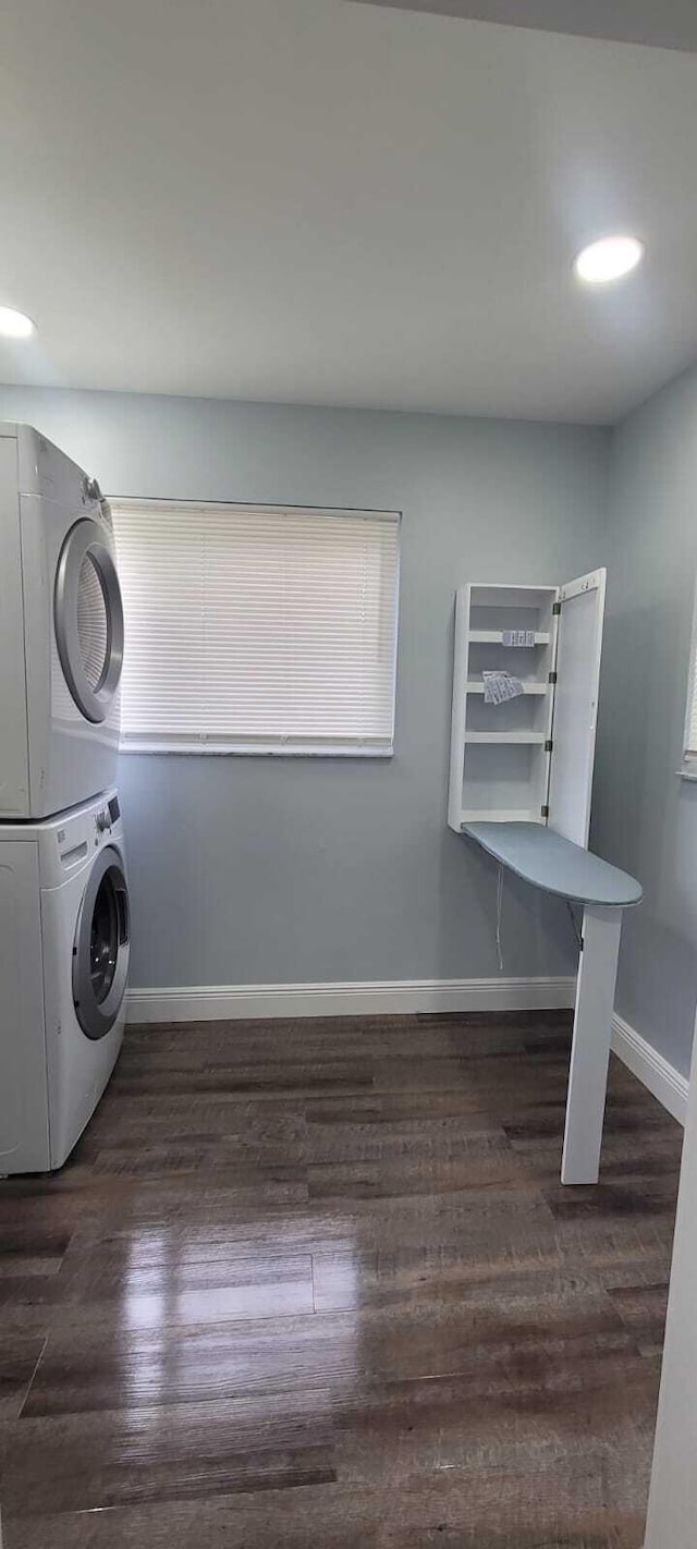 clothes washing area featuring recessed lighting, stacked washer / dryer, baseboards, wood finished floors, and laundry area