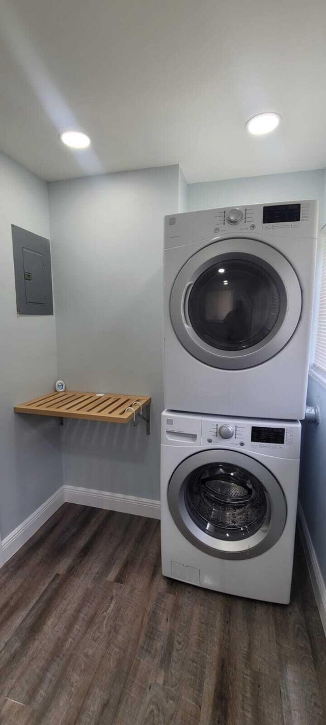 laundry room with baseboards, stacked washing maching and dryer, electric panel, dark wood-type flooring, and laundry area