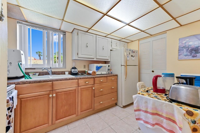 kitchen with white appliances, a sink, light tile patterned flooring, a drop ceiling, and dark countertops