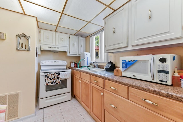 kitchen with white appliances, under cabinet range hood, a sink, light tile patterned floors, and white cabinets