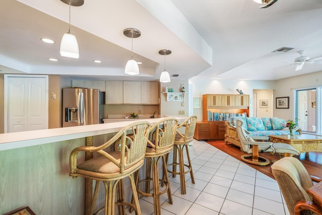kitchen with light tile patterned floors, stainless steel fridge, a breakfast bar, visible vents, and light countertops